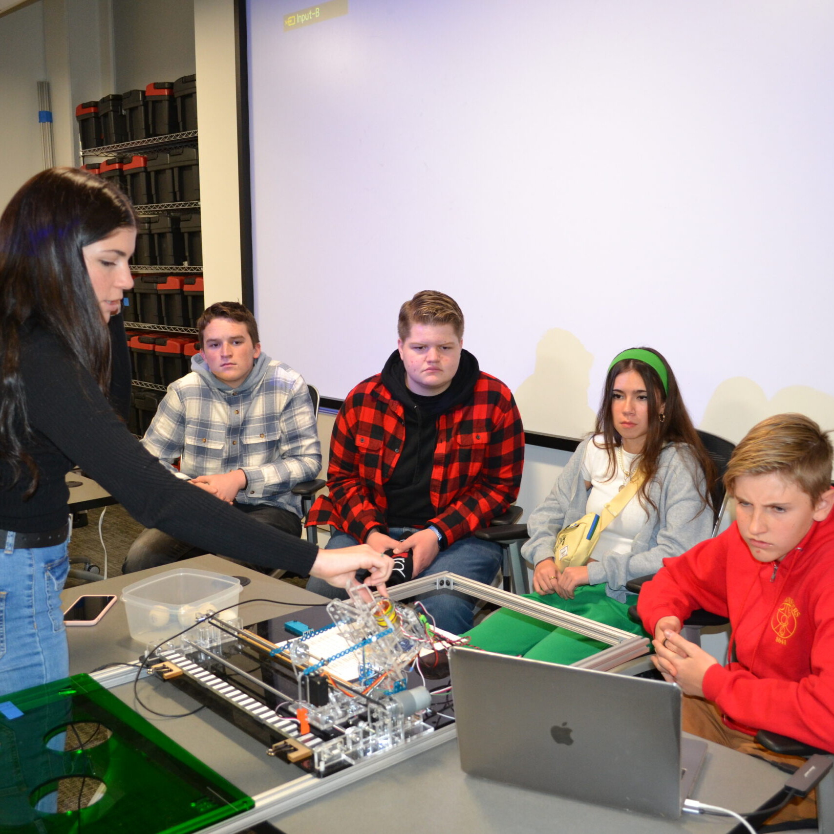 White woman with black hair shows four students electrical board